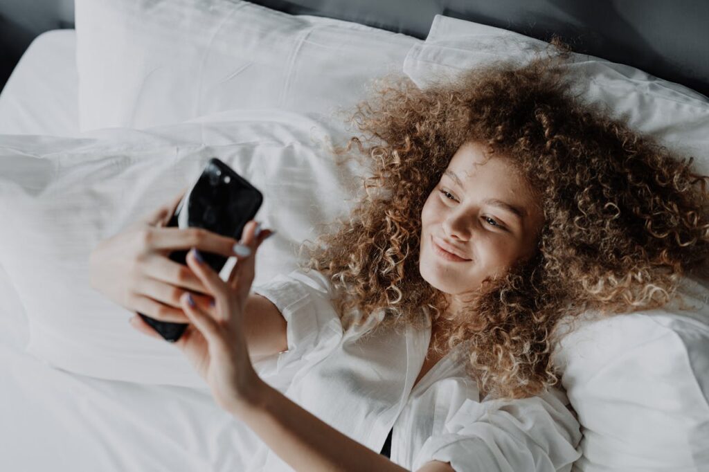 Donna con capelli ricci lunghi stesa sul letto che si fa un selfie