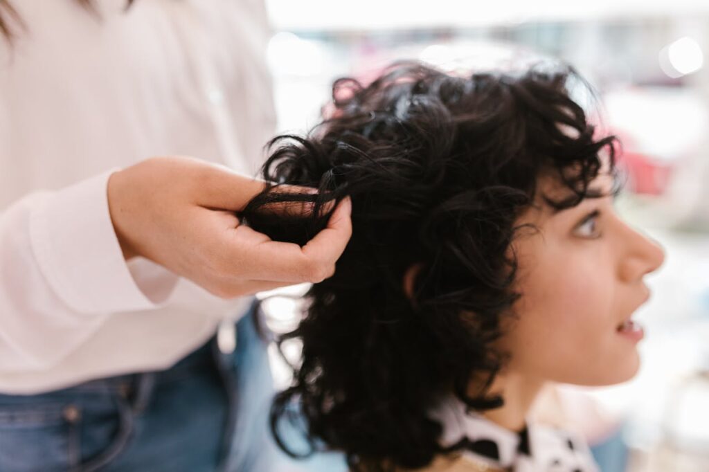 Parrucchiere lavora i capelli ricci neri di una donna